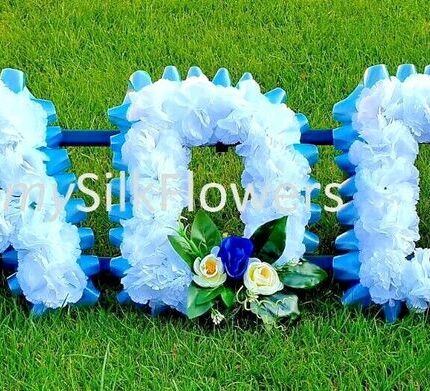 **DADDY Artificial Silk Funeral Tribute – Custom 5-Letter Name Flower Wreath (AUNTY Option)** Honor the memory of your loved one with this beautifully handcrafted **Artificial Silk Funeral Tribute Wreath**. Featuring a personalized 5-letter name, such as “DADDY” or “AUNTY,” this flower wreath is a meaningful and lasting tribute. Expertly made with premium artificial silk flowers, it offers a lifelike appearance and a thoughtful design, perfect for graveside or memorial displays. --- ### **Key Features:** #### **Personalized Name Tribute** - Customize your tribute with any **5-letter name**, including “DADDY,” “AUNTY,” or a name of your choice. - Each letter is adorned with vibrant artificial silk flowers, ensuring a visually striking and heartfelt tribute. #### **Premium Silk Flowers** - Crafted from high-quality **artificial silk carnations**, this wreath offers lasting beauty without the need for maintenance. - Enhanced with elegant **ribbon edging** and posy clusters, it adds a refined and personal touch. #### **Choice of Colors** - Select from **8 carnation colors** and **14 ribbon colors** to create a tribute that reflects the personality and style of your loved one. - Posy clusters are available in coordinating or contrasting colors to complete the design. #### **Ideal Dimensions** - Each tribute measures **XX inches wide x XX inches high**, providing a bold and graceful display for graveside or memorial settings. - Comes with a **florist frame stand** for easy setup and stability. #### **Complimentary Message Card** - Includes a **free message card and holder**, allowing you to express your love and condolences with a personalized note. --- ### **How to Order Your Custom Tribute:** 1. **Select a 5-Letter Name**: Choose “DADDY,” “AUNTY,” or any custom 5-letter name. 2. **Pick Carnation Colors**: Refer to Step 1 image and select from colors like White, Pink, Red, Purple, Yellow, and more. 3. **Choose Ribbon Colors**: Refer to Step 2 image and select from options like Baby Pink, Navy Blue, Gold, Black, Silver, and others. 4. **Add Posy Details**: Select the color of the posy cluster to complement your chosen design. 5. **Provide Personalization**: Use the “Personalization” box to specify your custom name, carnation color, ribbon color, and posy details. --- ### **Examples of Custom Orders:** - **Option 1:** Letters – DADDY Carnations – White Ribbon – Navy Blue Posy – Purple - **Option 2:** Letters – AUNTY Carnations – Pink Ribbon – Silver Posy – Yellow --- ### **Important Notes:** - **Color Variations**: Slight differences in colors may occur due to lighting during photography. We strive to ensure the final product matches your chosen colors as closely as possible. - **Floral Styles**: Occasionally, flower styles may vary slightly, but we ensure the overall design and quality remain consistent with the images provided. --- ### **Why Choose a Custom Artificial Silk Funeral Tribute?** This **DADDY Artificial Silk Funeral Tribute** is a thoughtful and elegant way to celebrate the life of a loved one. Designed for durability and beauty, it serves as a lasting symbol of love, remembrance, and respect. Perfect for graveside services, memorials, or as a keepsake, this tribute provides comfort and heartfelt meaning during difficult times.